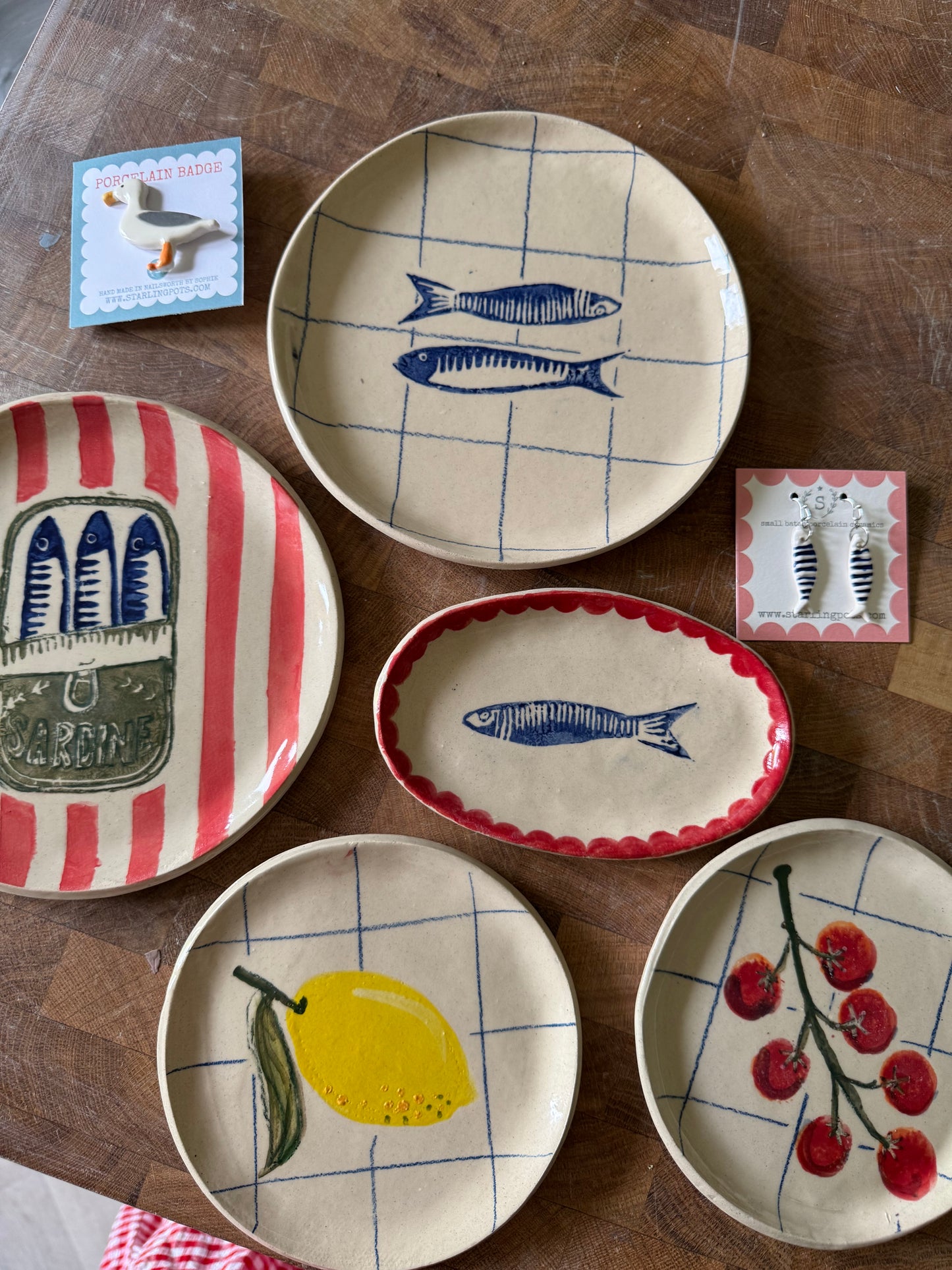 Collection of handmade ceramic plates including sardine oval dish on wooden surface
