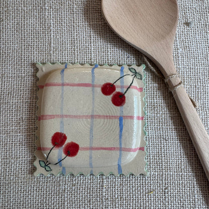 Handmade ceramic ravioli shaped spoon rest with cherry design on linen background