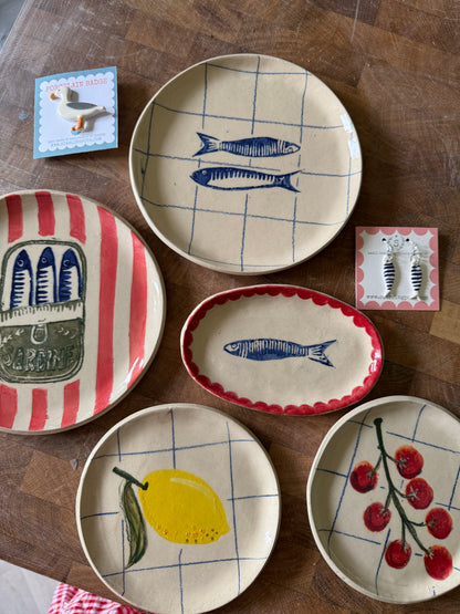Collection of handmade ceramic plates including sardine oval dish on wooden surface