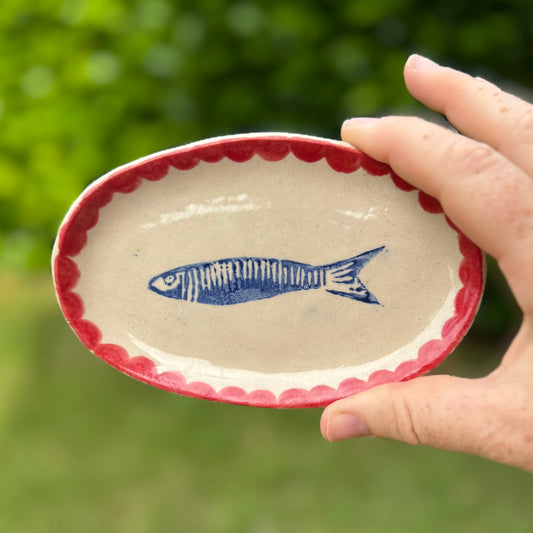 Handmade ceramic sardine oval dish with red scalloped edge held outdoors