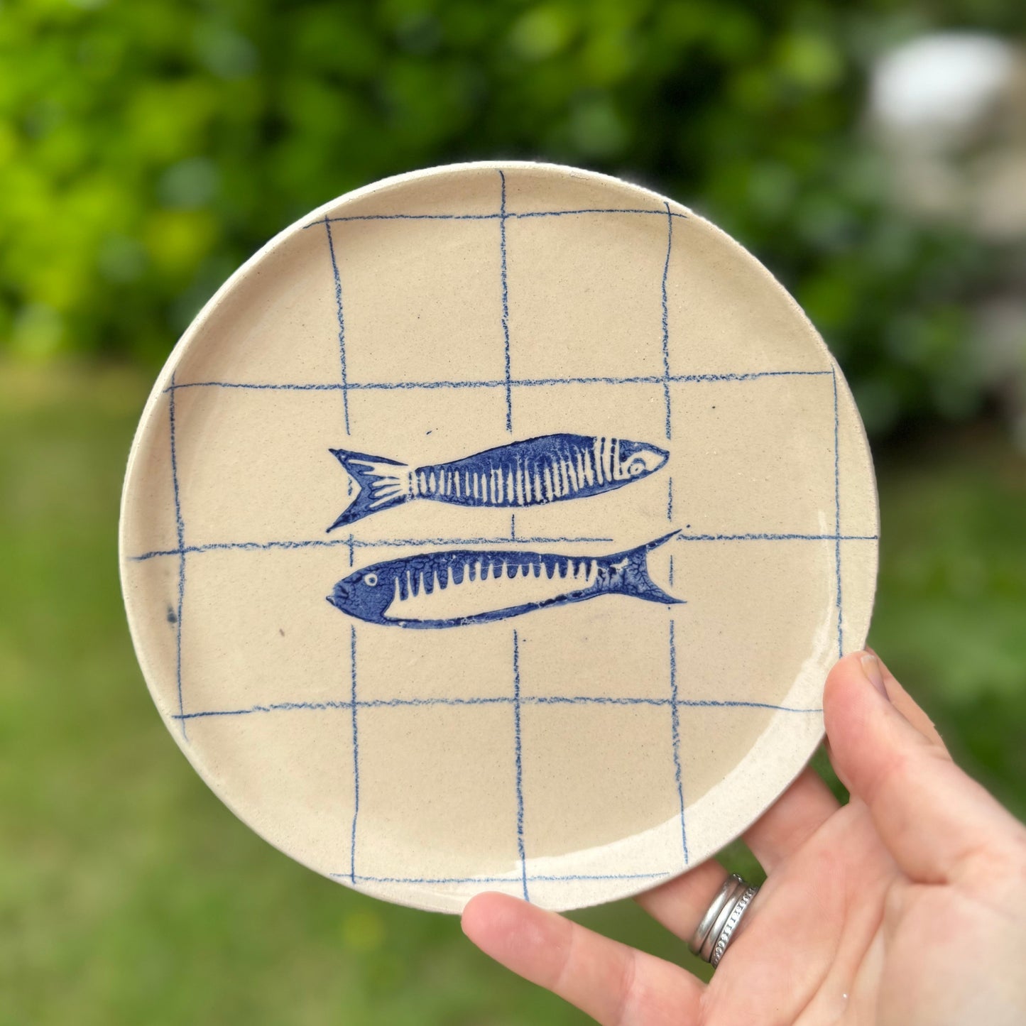 Handmade ceramic sardine pair plate with cobalt blue grid design held outdoors
