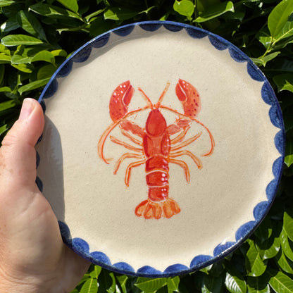 Handmade ceramic lobster platter with cobalt blue scalloped edge held against green leaves