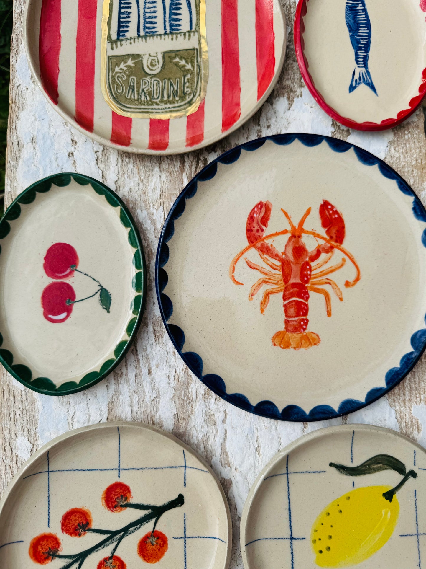 Collection of handmade ceramic plates including cherry oval dish on white surface