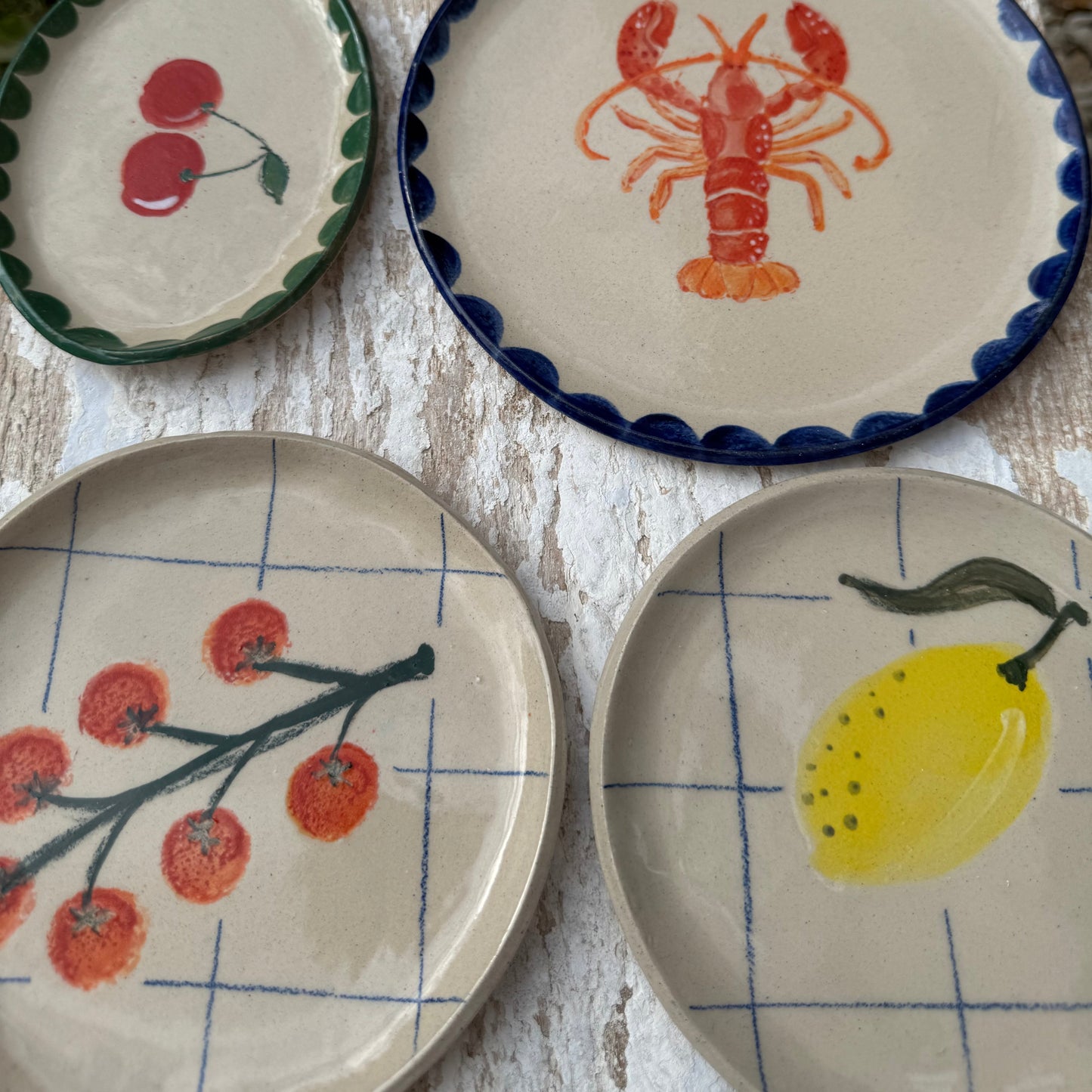 Collection of handmade ceramic plates including lemon and tomato designs on white surface