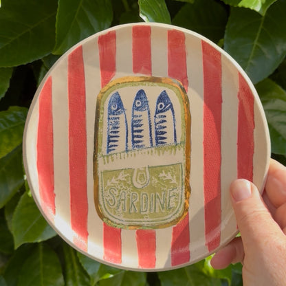 Handmade ceramic sardine tin plate held up against green leaves